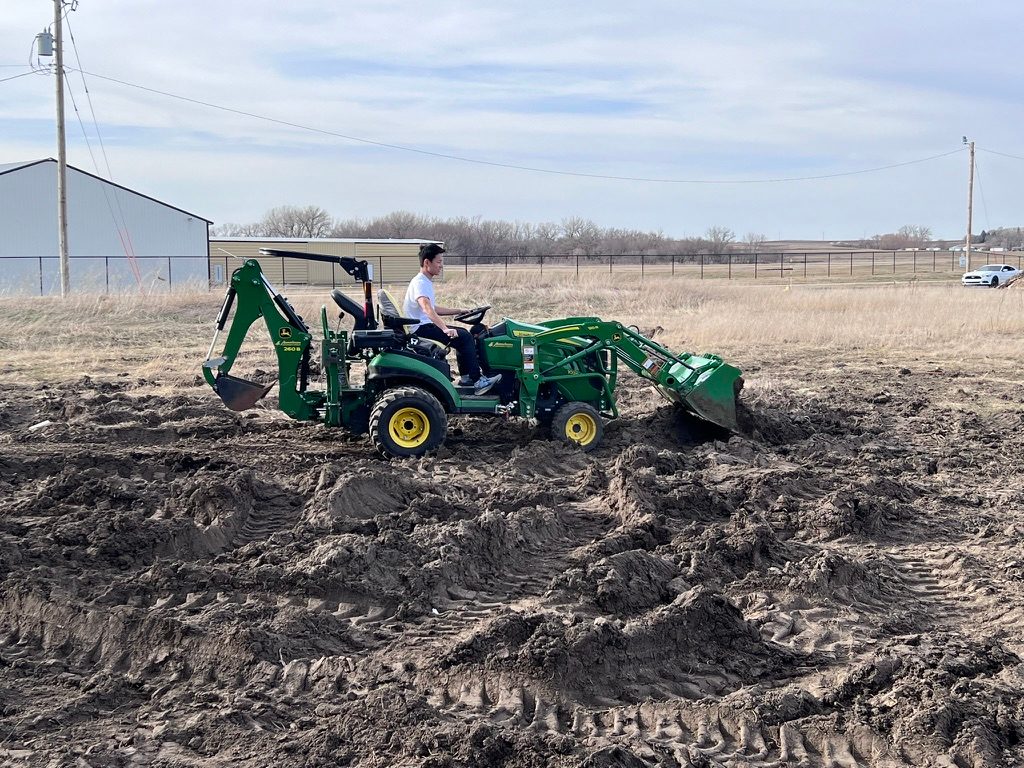 A person seated on a green tractor in a muddy field